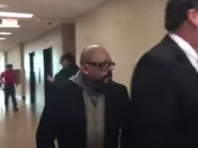 AB Quintanilla is wearing a black coat in the picture as he walks towards the room.